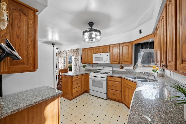 kitchen with a sink, dark stone countertops, white appliances, a peninsula, and brown cabinetry