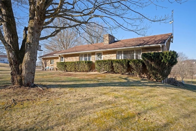 view of front facade featuring brick siding, a chimney, and a front yard