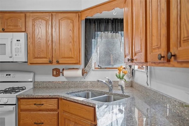 kitchen with white appliances, light stone countertops, brown cabinets, and a sink