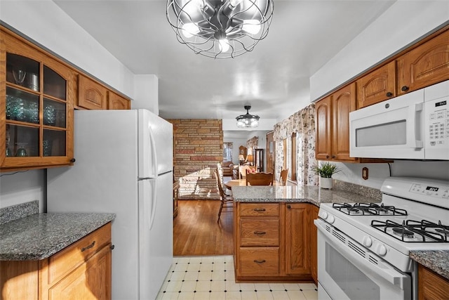 kitchen featuring white appliances, brown cabinetry, light floors, glass insert cabinets, and a chandelier