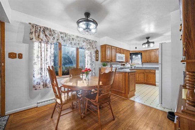 dining space featuring a wealth of natural light, a baseboard radiator, baseboards, and light wood-style flooring