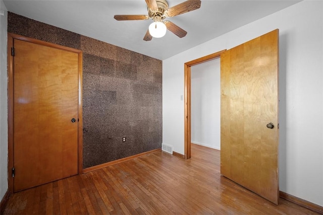 unfurnished bedroom featuring visible vents, wood-type flooring, baseboards, and an accent wall