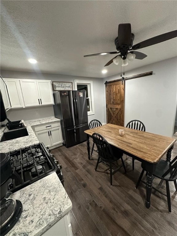 kitchen with dark wood-type flooring, black appliances, a sink, a barn door, and white cabinets