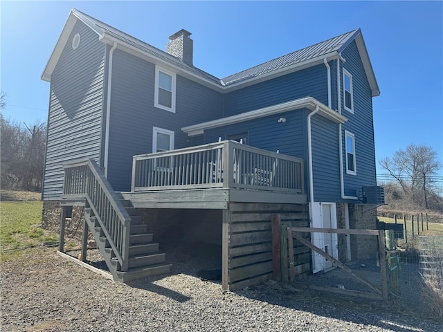 back of house featuring a wooden deck, a standing seam roof, a chimney, stairs, and metal roof