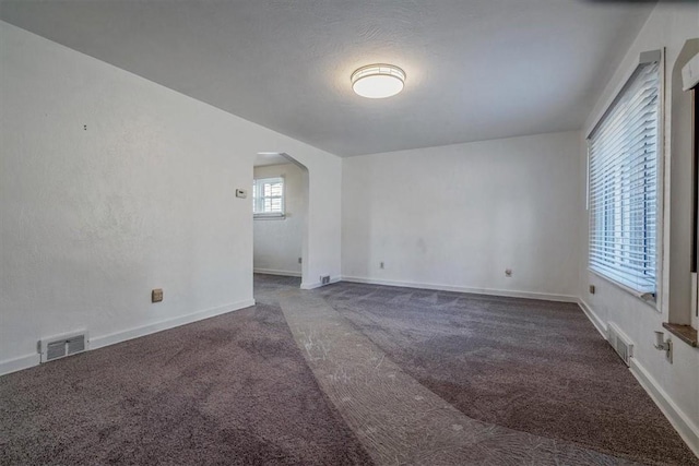 empty room with carpet, arched walkways, visible vents, and baseboards