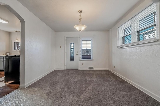 foyer entrance featuring dark colored carpet, visible vents, arched walkways, and baseboards