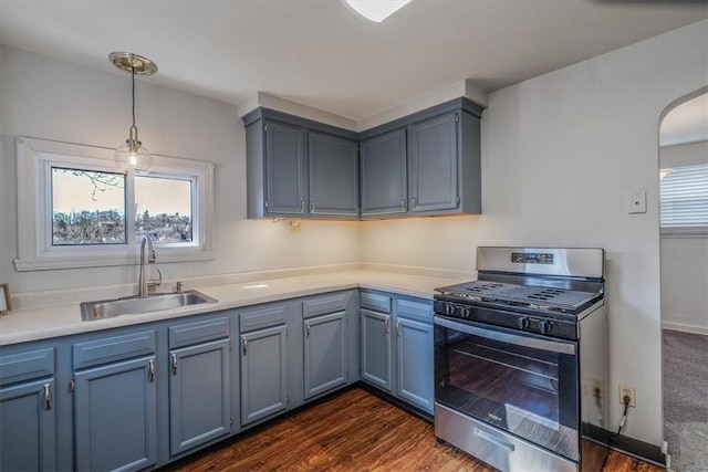 kitchen featuring a sink, decorative light fixtures, arched walkways, light countertops, and gas range