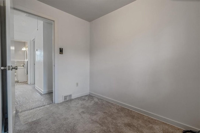 carpeted spare room featuring visible vents, attic access, and baseboards