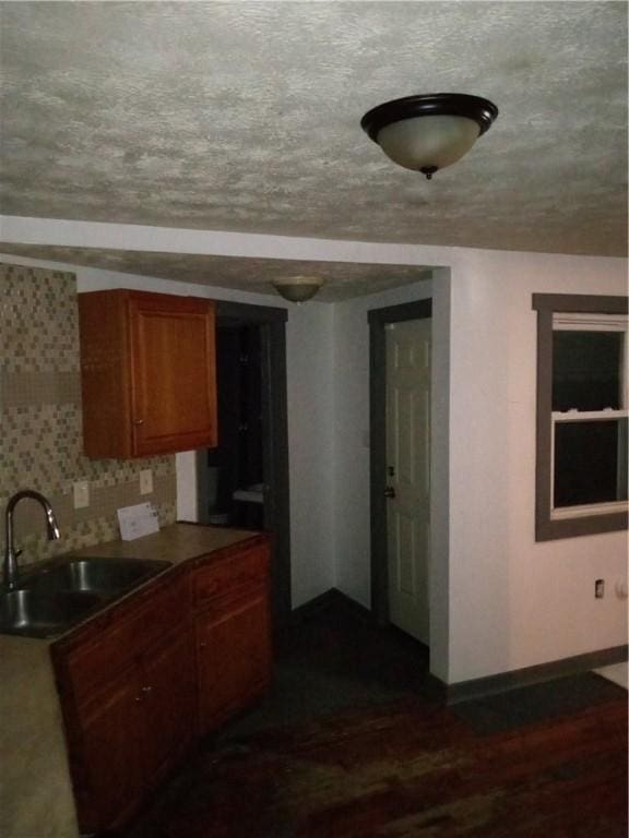 kitchen with baseboards, dark wood finished floors, decorative backsplash, brown cabinetry, and a sink