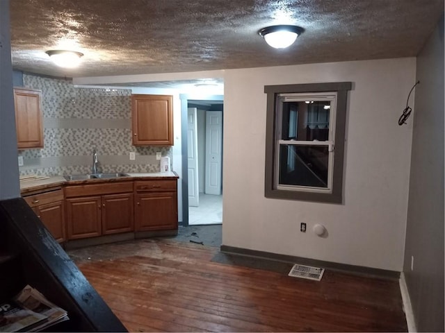 kitchen featuring wood finished floors, visible vents, baseboards, a sink, and a textured ceiling