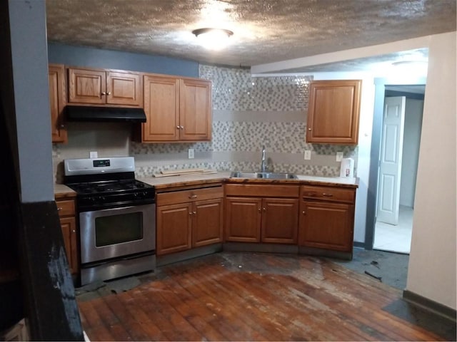 kitchen featuring a sink, under cabinet range hood, light countertops, stainless steel gas range, and dark wood-style flooring