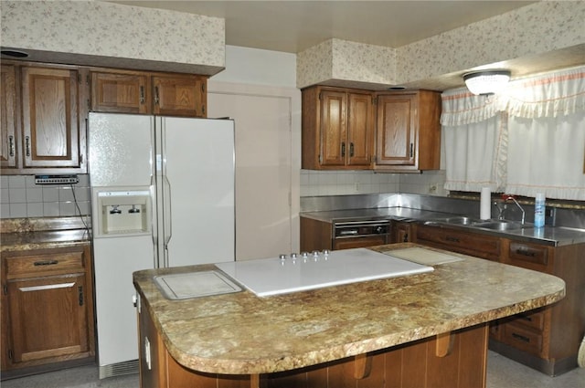 kitchen featuring tasteful backsplash, a center island, white refrigerator with ice dispenser, brown cabinetry, and a sink