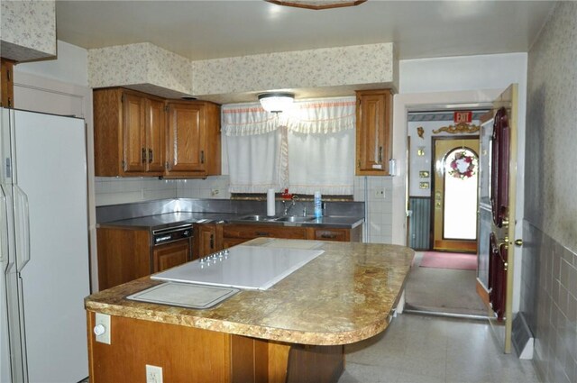 kitchen featuring brown cabinetry, a kitchen island, wallpapered walls, freestanding refrigerator, and a sink