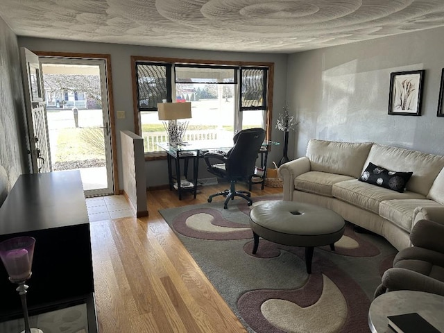 living room with a wealth of natural light, baseboards, light wood-style floors, and a textured ceiling