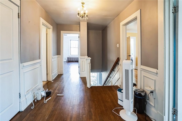 hall with a wainscoted wall, an upstairs landing, dark wood-type flooring, radiator, and an inviting chandelier