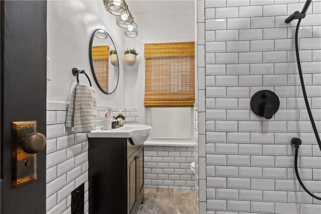 bathroom with a tile shower, a wainscoted wall, vanity, and tile walls