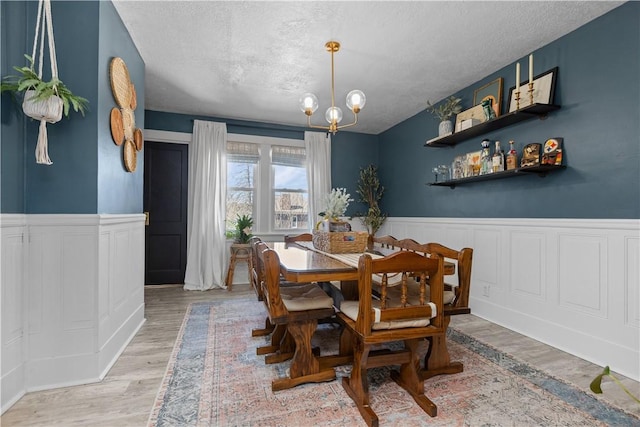 dining room featuring a chandelier, a wainscoted wall, a textured ceiling, and light wood-type flooring