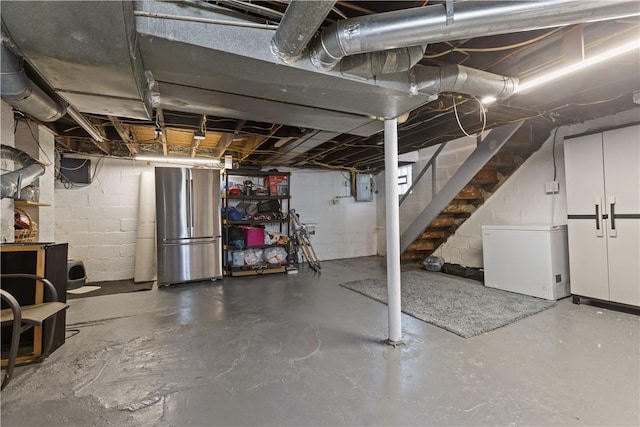 unfinished basement with fridge, electric panel, stairs, and freestanding refrigerator