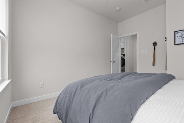 bedroom featuring baseboards, light carpet, multiple windows, and washer / dryer