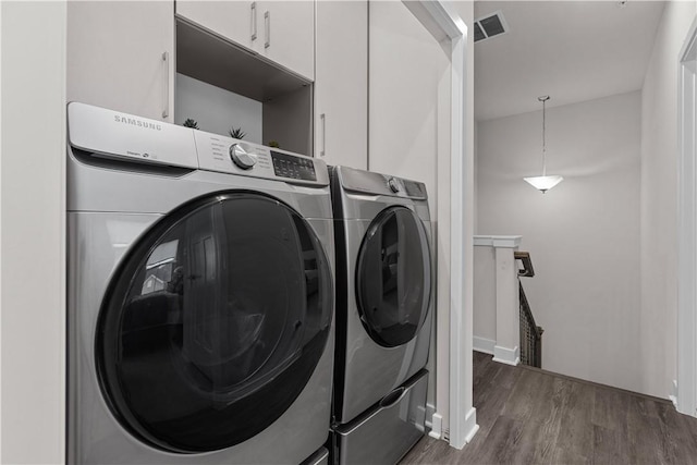 washroom featuring dark wood-style floors, visible vents, washing machine and dryer, and cabinet space