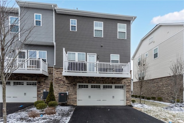 back of house featuring aphalt driveway, stone siding, central air condition unit, and a garage