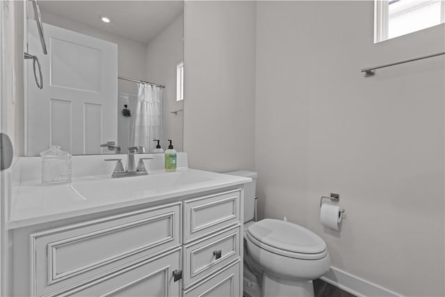 bathroom with a wealth of natural light, baseboards, toilet, and vanity