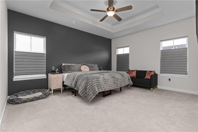 bedroom featuring light colored carpet, baseboards, a tray ceiling, and a ceiling fan