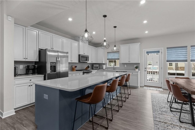 kitchen with stainless steel appliances, wood finished floors, a kitchen island, and white cabinets