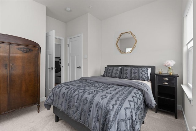 bedroom with stacked washer and dryer, light colored carpet, and baseboards