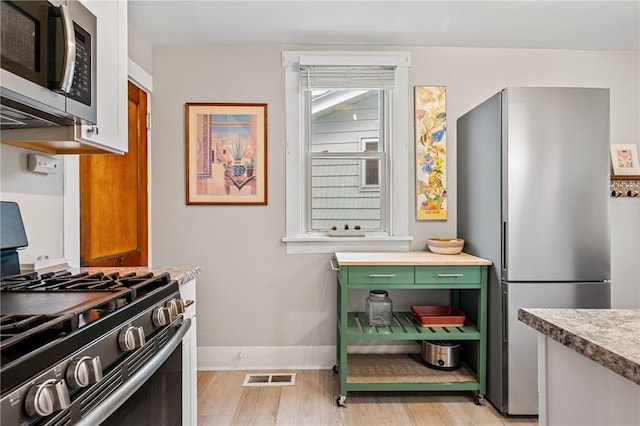 kitchen with baseboards, light wood finished floors, visible vents, green cabinetry, and appliances with stainless steel finishes