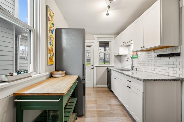 kitchen featuring light wood finished floors, stainless steel appliances, a sink, white cabinetry, and tasteful backsplash