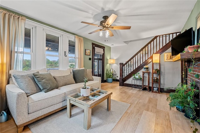 living area featuring stairway, light wood-style flooring, and a ceiling fan