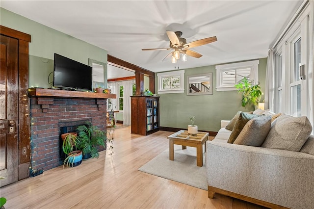 living area featuring a brick fireplace, baseboards, ceiling fan, and wood finished floors