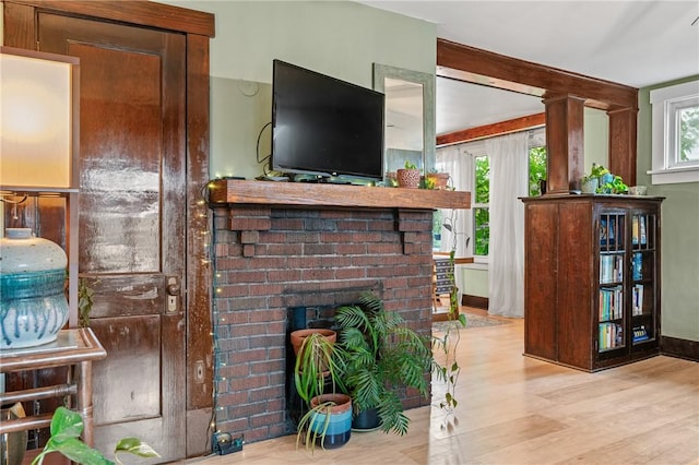 living area featuring wood finished floors, a brick fireplace, and a healthy amount of sunlight