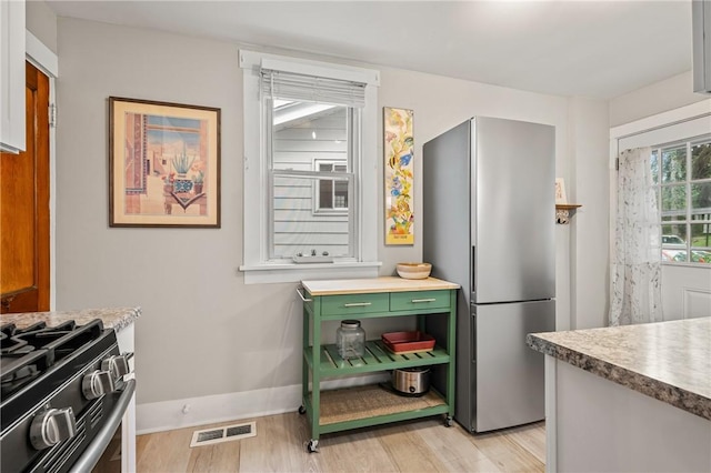 kitchen featuring visible vents, light wood finished floors, range with gas cooktop, freestanding refrigerator, and green cabinets