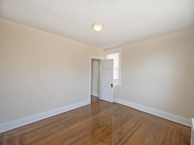 spare room featuring wood finished floors, baseboards, a textured wall, and a textured ceiling