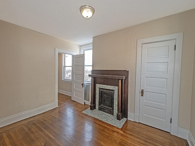 unfurnished living room featuring a tiled fireplace, baseboards, and wood finished floors