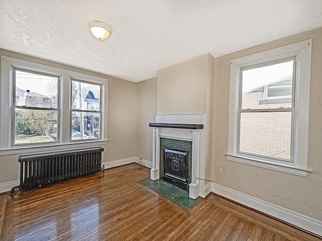 unfurnished living room featuring dark wood-type flooring, radiator heating unit, baseboards, and a textured ceiling