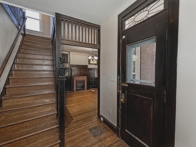 foyer entrance featuring visible vents, a fireplace with flush hearth, stairs, baseboards, and dark wood-style flooring