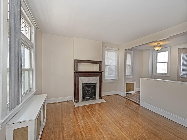 unfurnished living room with a fireplace with flush hearth, light wood-style floors, and baseboards