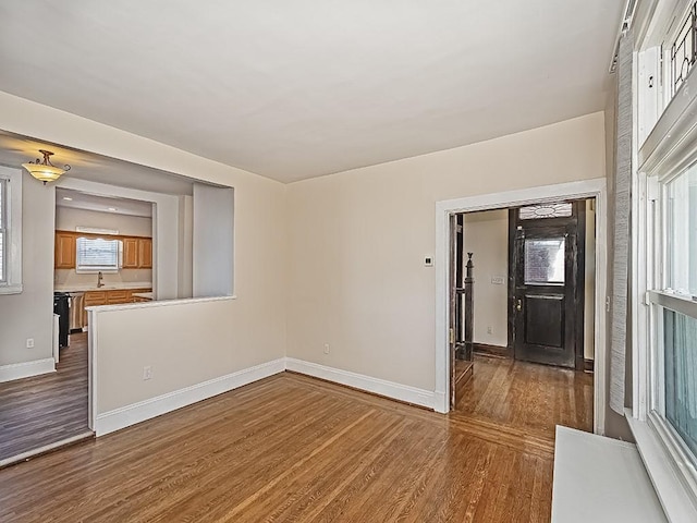 unfurnished living room featuring wood finished floors, baseboards, and a sink