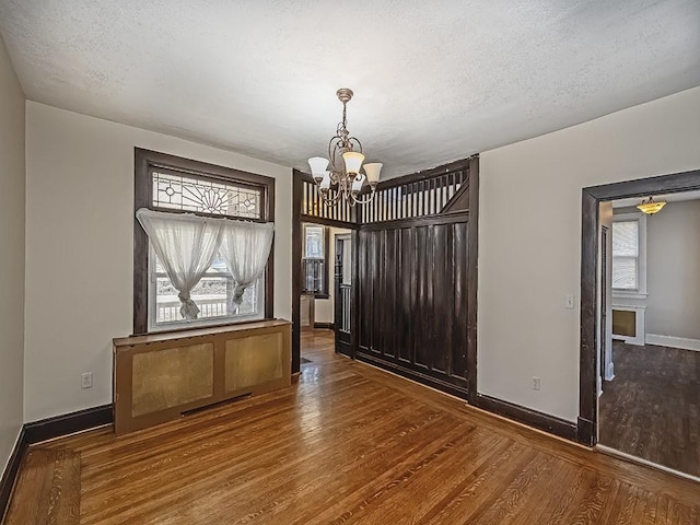 unfurnished dining area featuring visible vents, baseboards, wood finished floors, a notable chandelier, and a textured ceiling