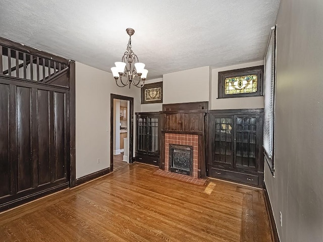 unfurnished living room featuring a fireplace with flush hearth, wood finished floors, baseboards, and a textured ceiling