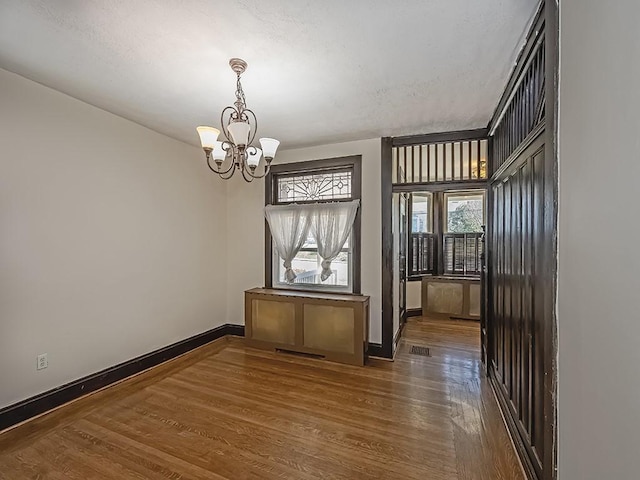 unfurnished dining area with a chandelier, baseboards, and wood finished floors