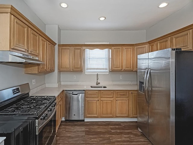 kitchen with dark wood-type flooring, under cabinet range hood, a sink, appliances with stainless steel finishes, and light countertops