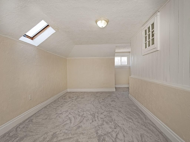 additional living space featuring vaulted ceiling with skylight, a textured ceiling, carpet flooring, and a textured wall