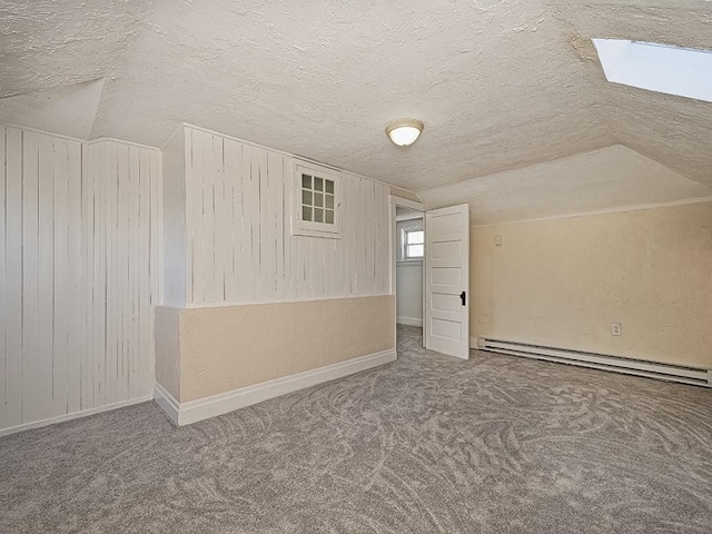 additional living space with lofted ceiling with skylight, a textured ceiling, a baseboard heating unit, and carpet