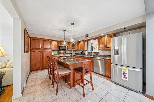 kitchen with brown cabinets, a center island with sink, a sink, appliances with stainless steel finishes, and a breakfast bar area