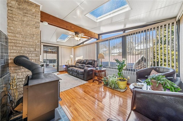 sunroom / solarium with vaulted ceiling with skylight, ceiling fan, and a wood stove