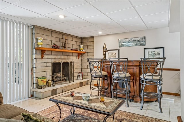 living area featuring light tile patterned floors, baseboards, a drop ceiling, a dry bar, and a large fireplace